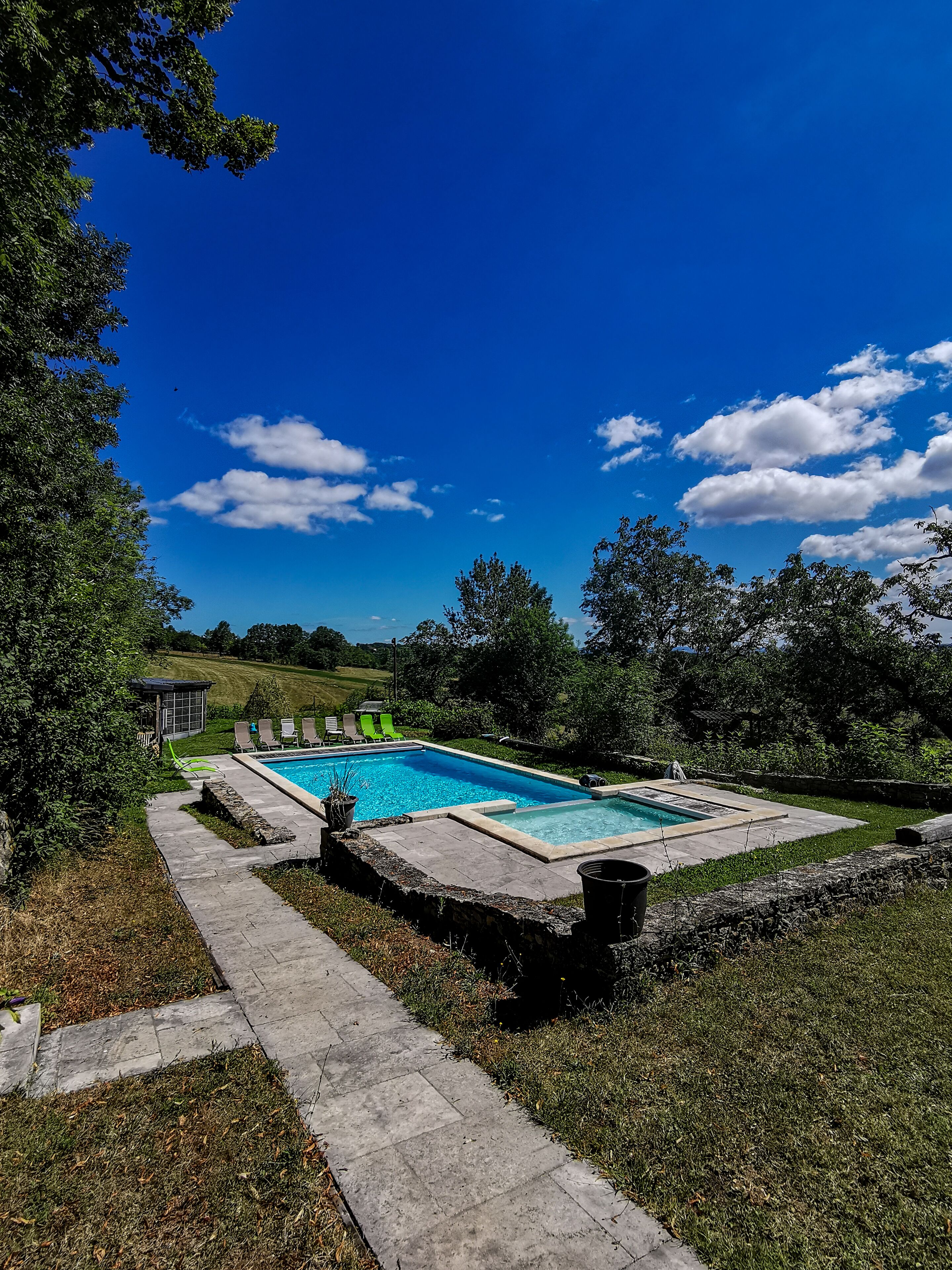 Piscina rectangular con borde de piedra, rodeada por un muro de piedra y una zona ajardinada.