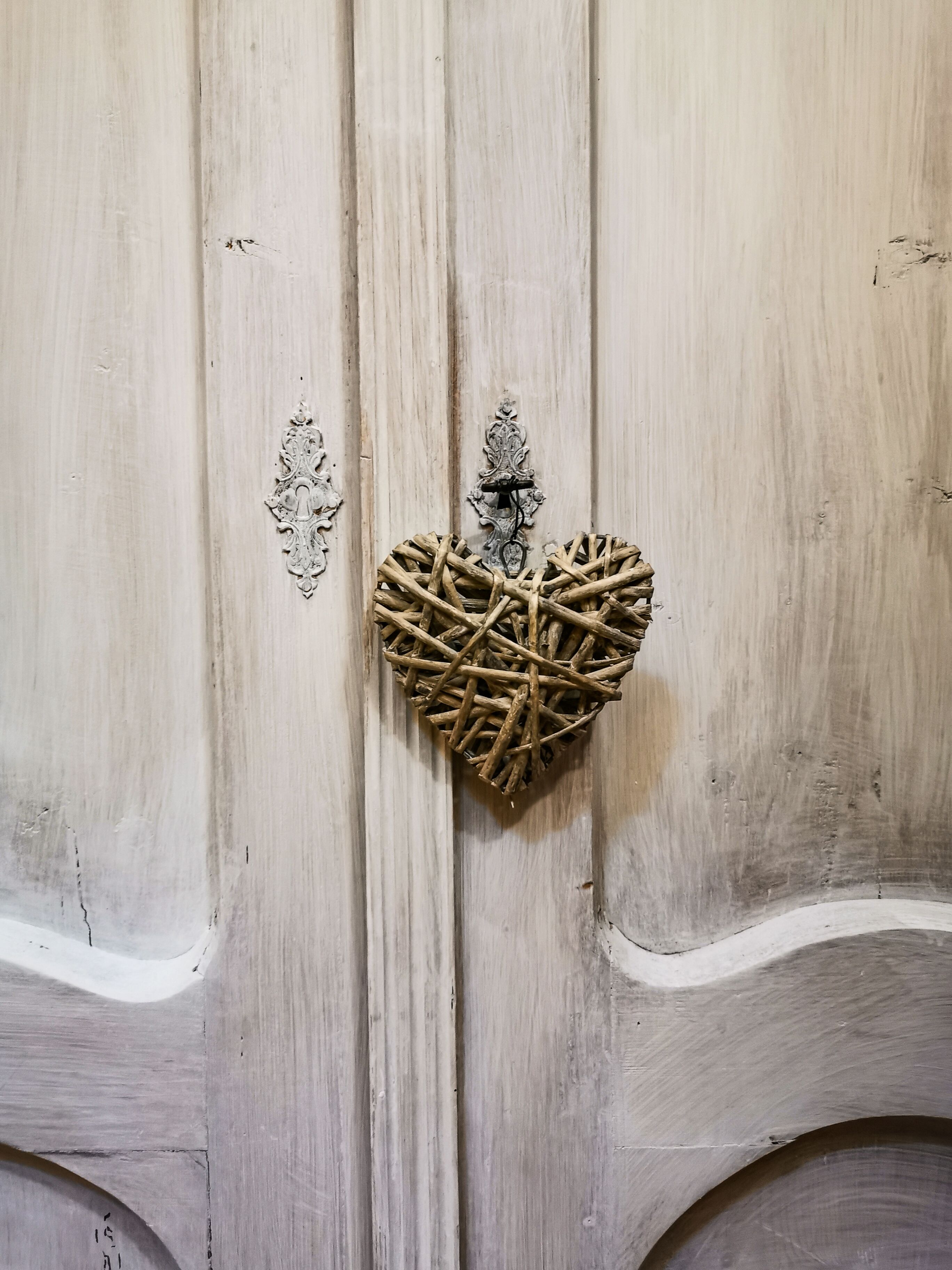 Une porte en bois ornée d’un motif en forme de cœur, réalisé à partir de brindilles, et dotée d’un loquet en métal.
