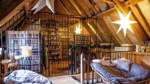 Ein gemütliches Dachzimmer mit hohen Decken, einer sternförmigen Lampe, einem Bücherregal, einem Korbstuhl und einem Bett mit blauer Steudecke.