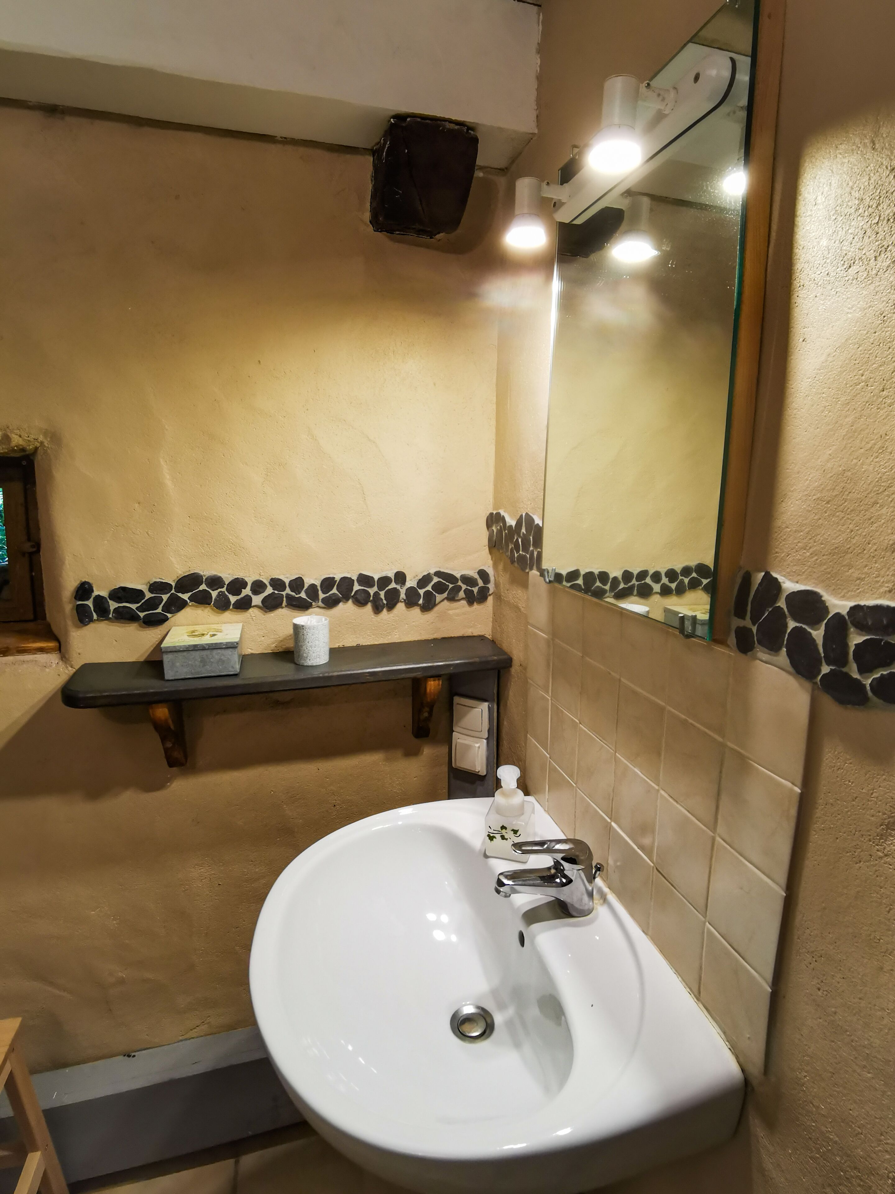 Une salle de bain avec un lavabo blanc, un miroir, une étagère contenant des articles de toilette et une bordure en mosaïque de pierre.