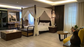 A spacious bedroom with a four-poster bed, a sitting area with a chair and table, a bedside table with a lamp, and a large mirror. - Merry Season Motel (Kaohsiung)