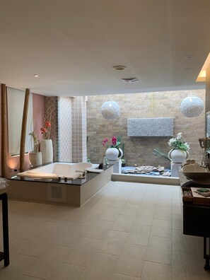 Une salle de bain moderne avec une grande baignoire, un espace douche séparé et un petit lavabo. On y trouve des éléments décoratifs, comme des plantes en pot et un luminaire sphérique fixé au mur.