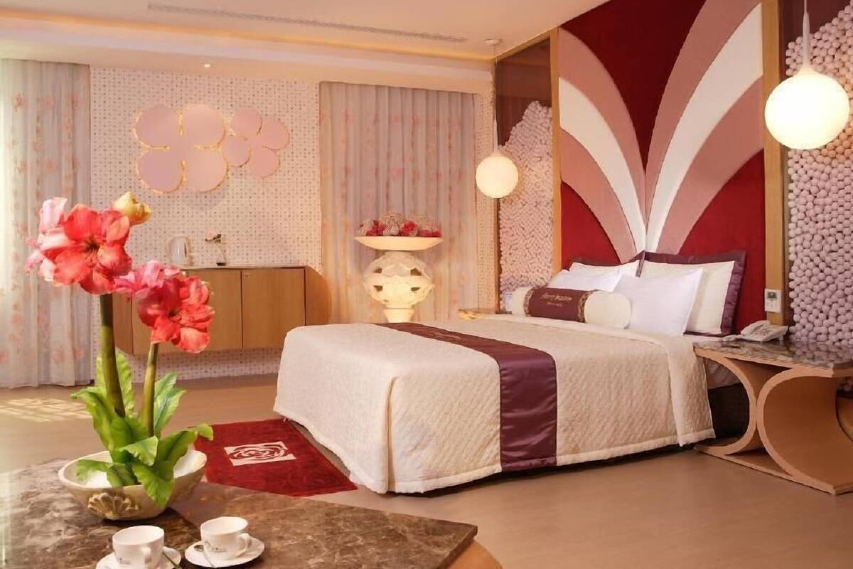 Une chambre d’hôtel comprenant un lit, une table de chevet, une lampe, un mur décoratif et une plante.
