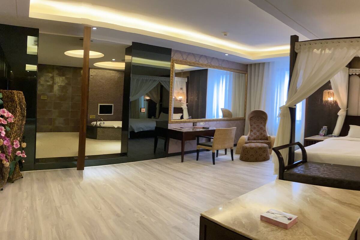 Une chambre d’hôtel moderne avec un lit, un canapé jaune, une petite table et un miroir.