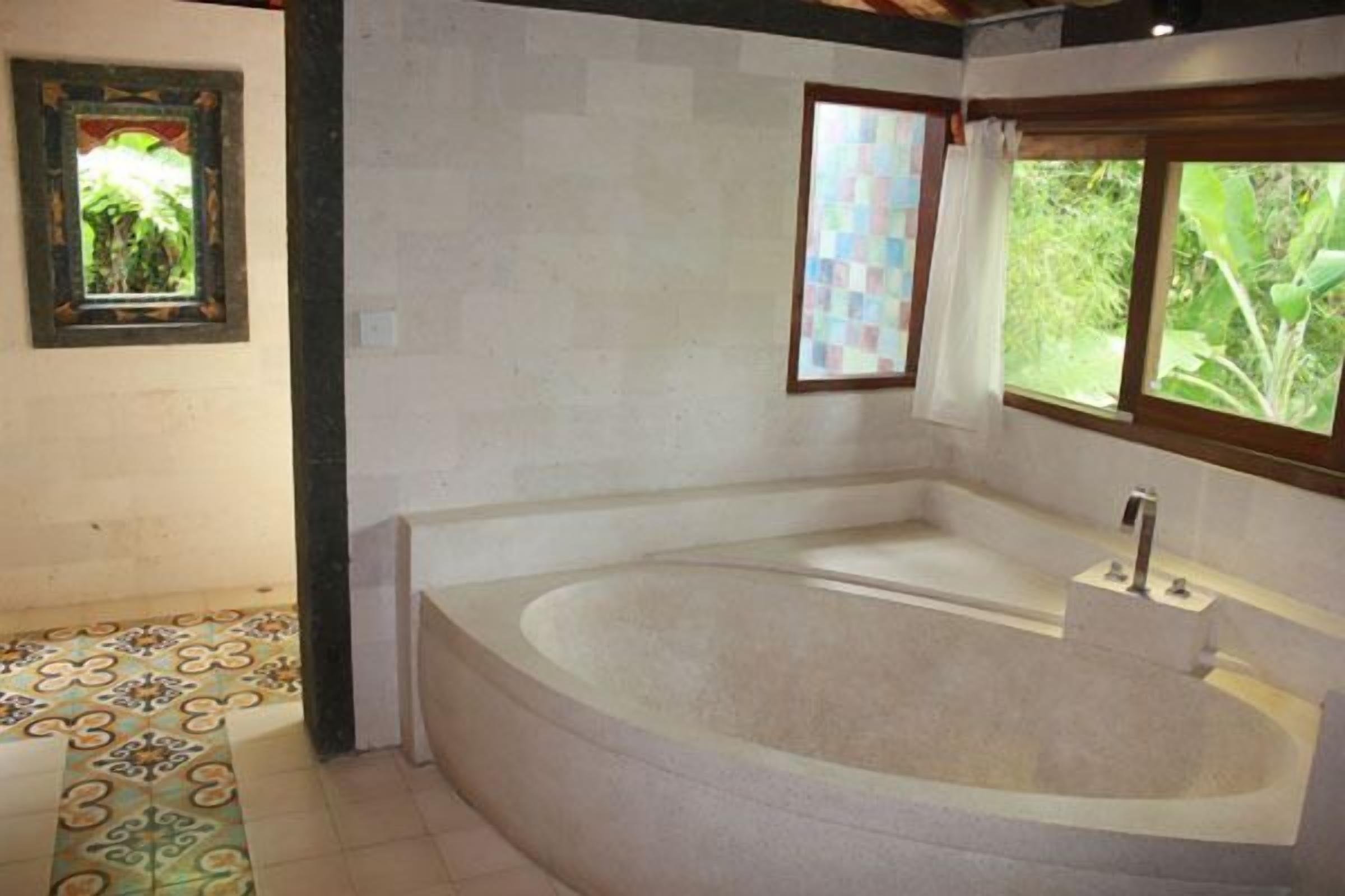 Un baño con una bañera independiente grande, una ventana con vistas a zonas verdes y baldosas de suelo estampadas.
