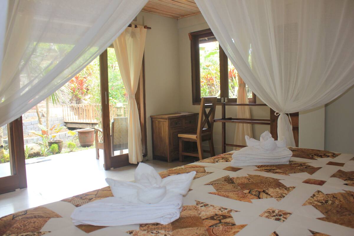 Un dormitorio con cama, una silla, un escritorio y una ventana con cortinas.