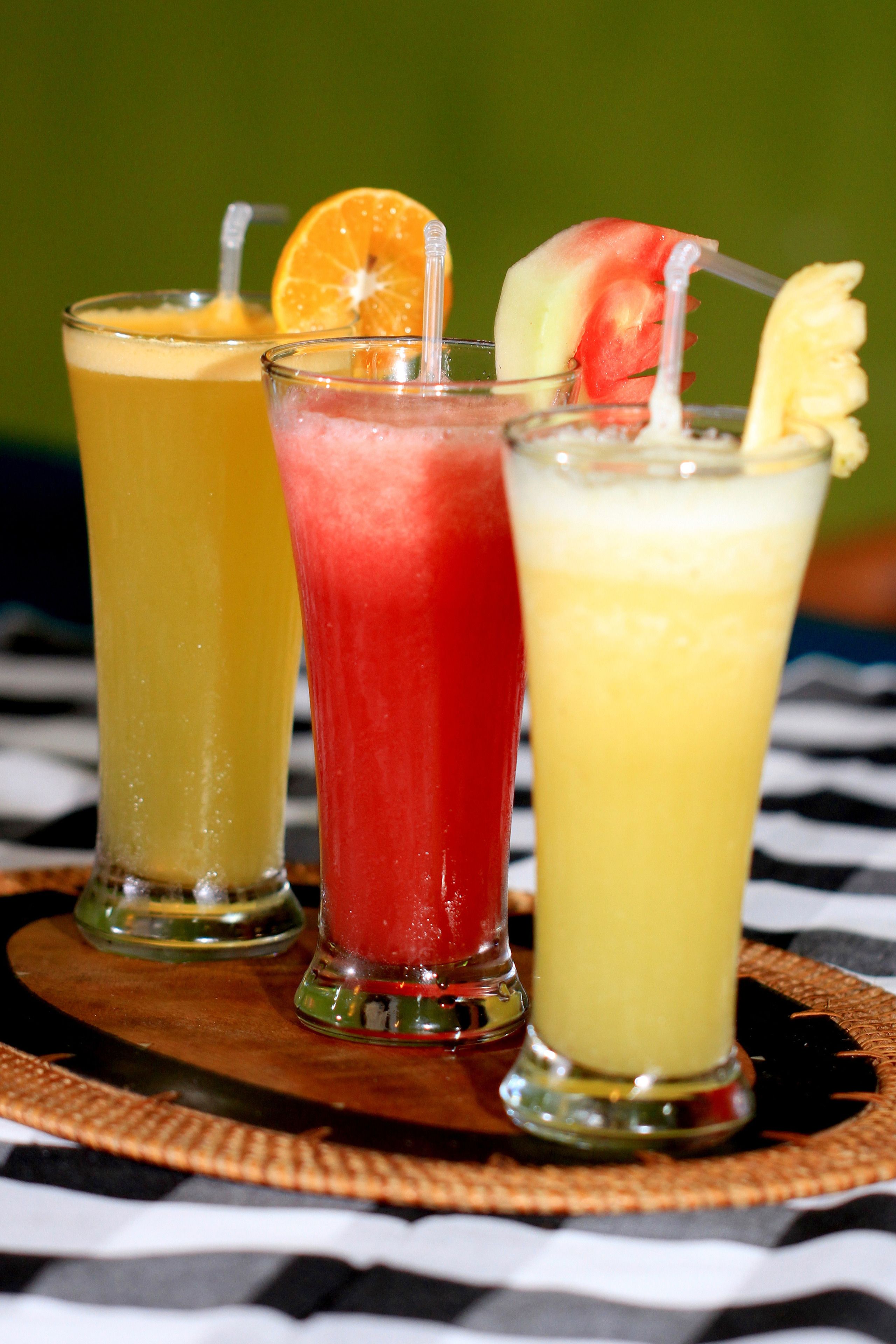 Tres vasos de cocteles con adornos de fruta sobre una estera trenzada.