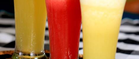 Tres vasos de cocteles con adornos de fruta sobre una estera trenzada.
