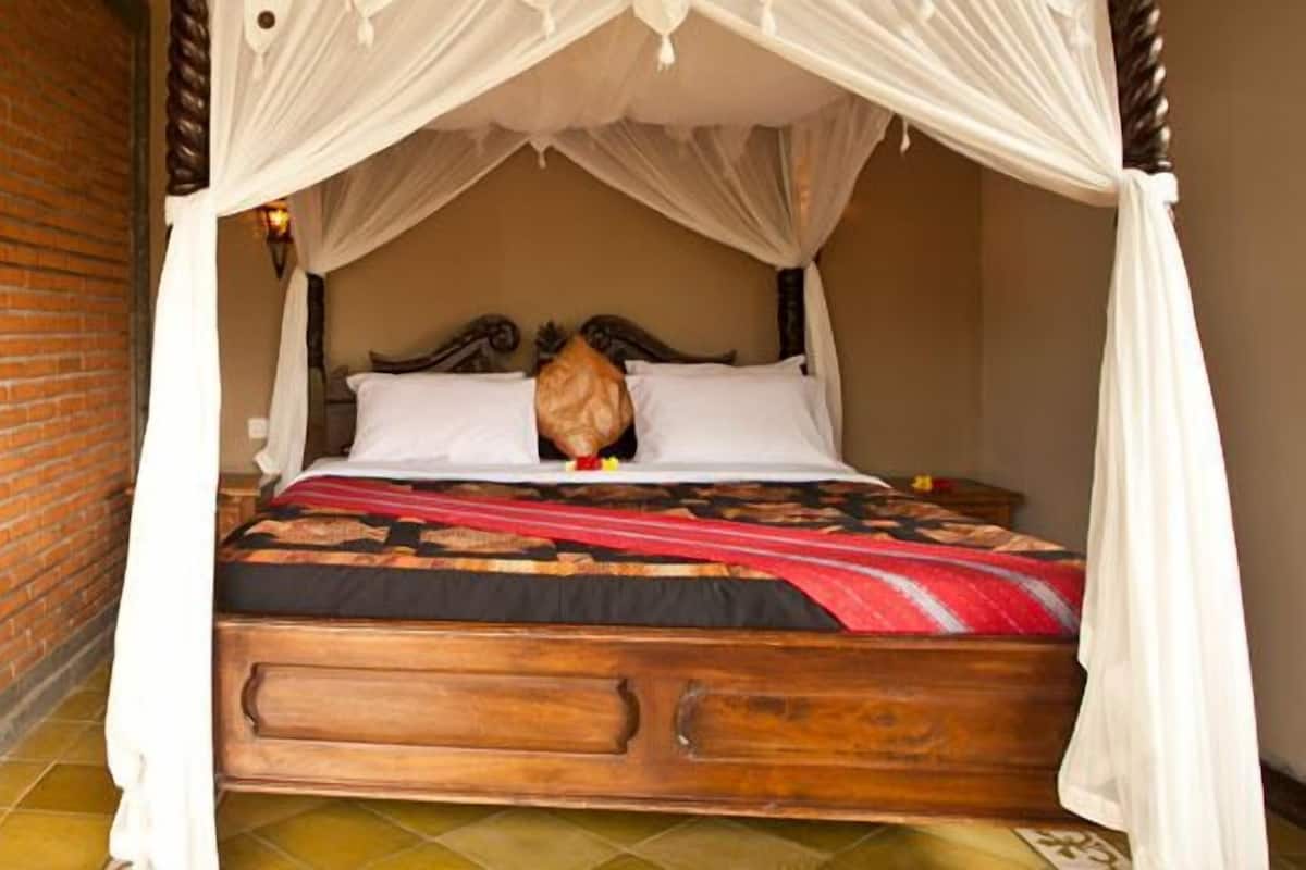 Una habitación con pared de ladrillo, cama de madera con dosel y una puerta decorativa.