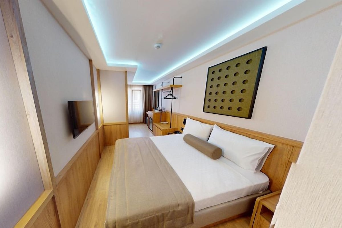 A hotel room with a bed, bedside table, lamp, and a TV.