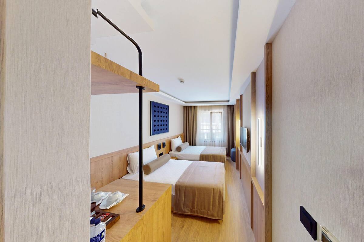 Une chambre d’hôtel avec un lit superposé, une table de chevet avec une lampe, un téléviseur fixé au mur et une grande fenêtre avec des rideaux.