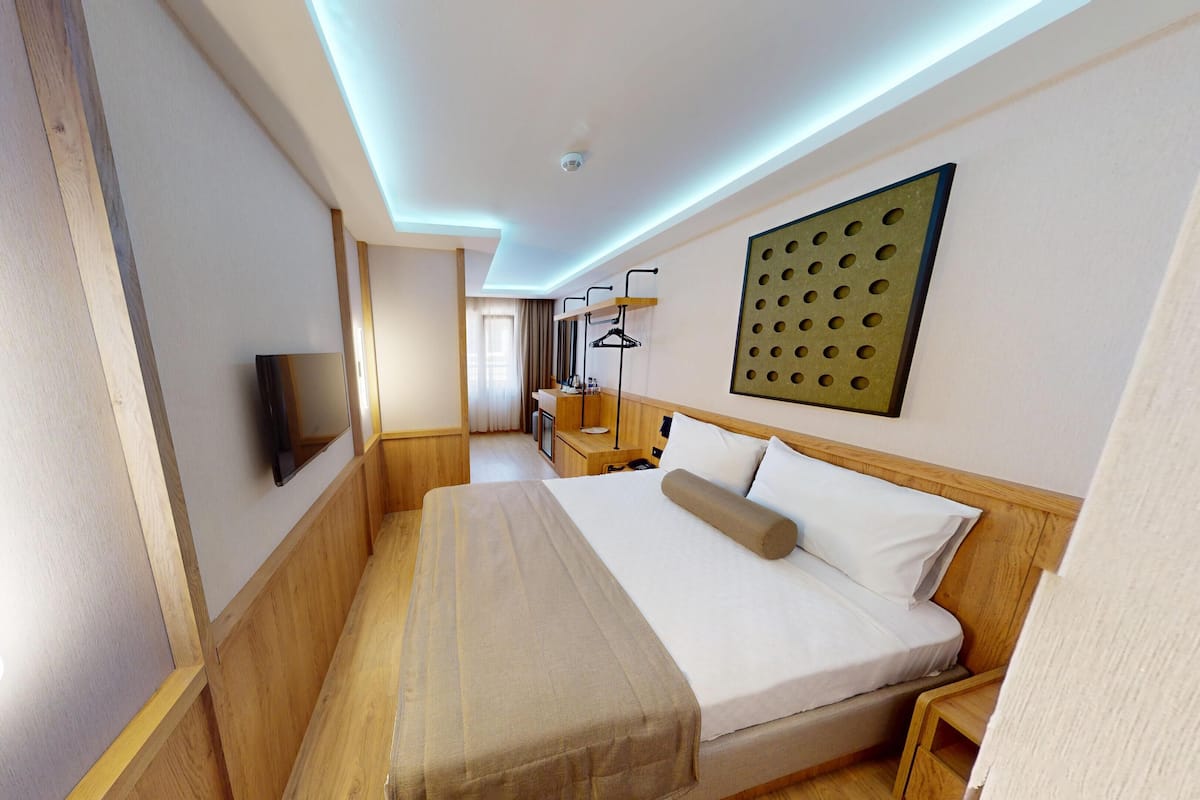 Une chambre d’hôtel avec un grand lit, un téléviseur fixé au mur, une tête de lit en bois et une petite table de chevet.
