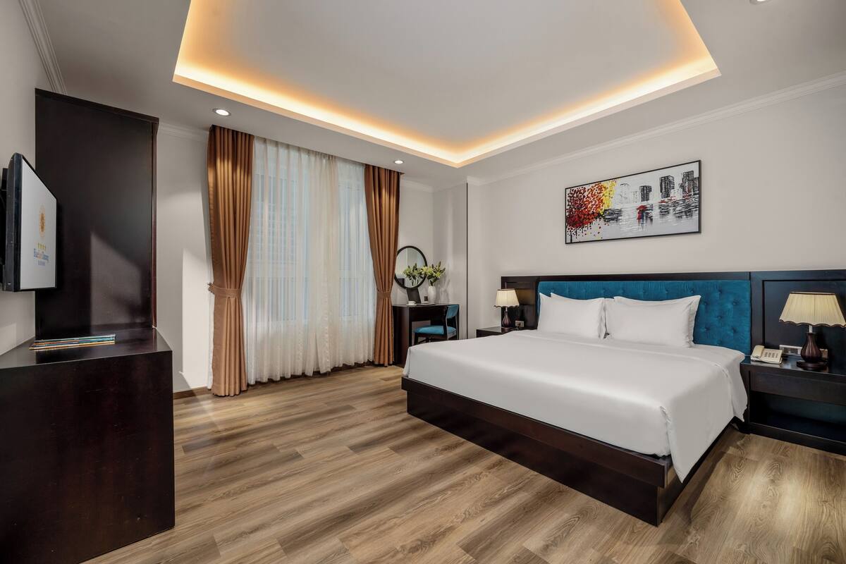 A modern hotel room with a large bed, a desk, a chair, and a TV.