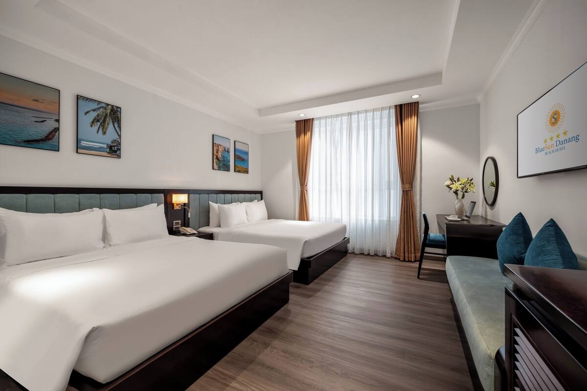 A hotel room with two beds, a desk, a chair, and a sofa.