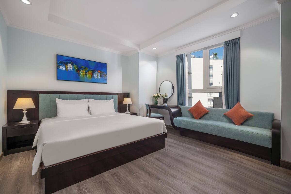 A hotel room with a large bed, a sofa, a desk, and a window with curtains.