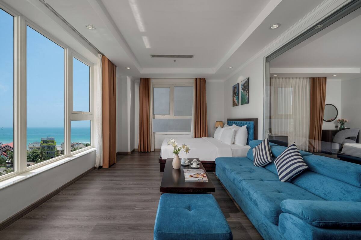 A hotel room with a large window, a bed, a blue sofa, and a coffee table.