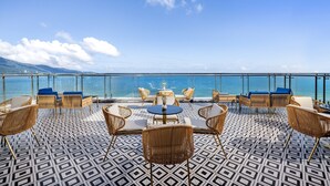 Una terraza con mobiliario de mimbre, piso estampado y vista al mar.