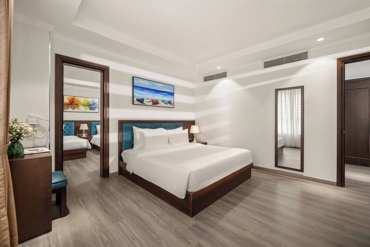 A hotel room with a large bed, a desk with a lamp, a mirror, and a painting on the wall.