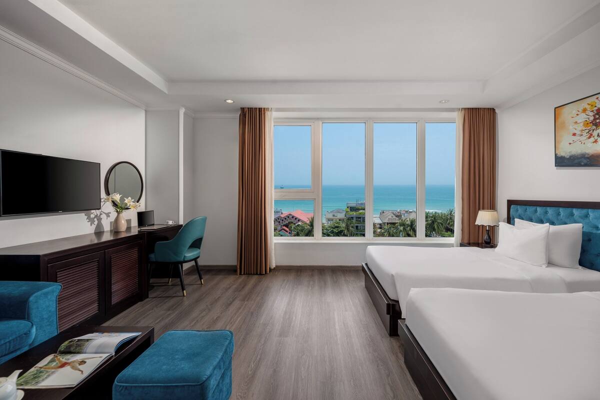 A hotel room with a large window, a bed, a desk, a chair, and a television.