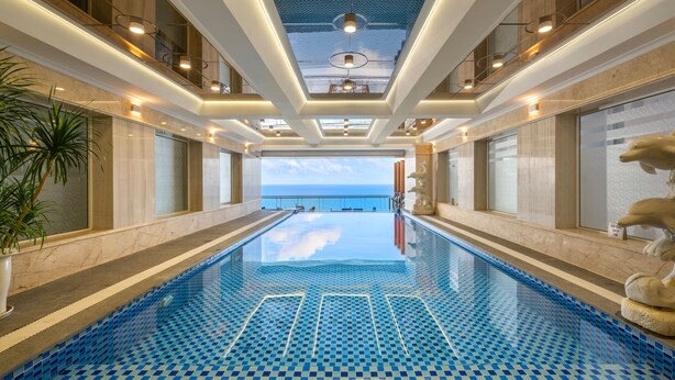 Una amplia piscina cubierta con vistas al mar, rodeada de paredes de mármol e iluminación moderna.