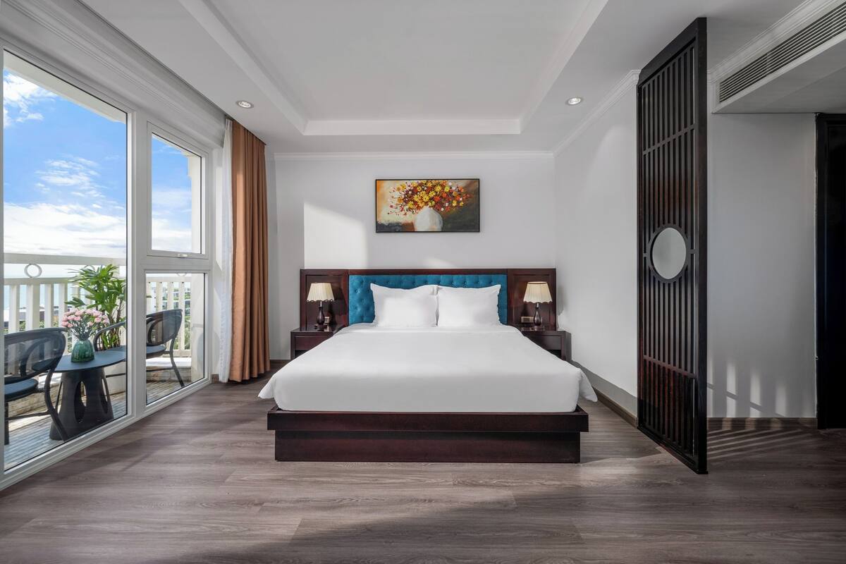 A spacious bedroom with a large bed, a view of the outdoors through a sliding door, and a painting on the wall.