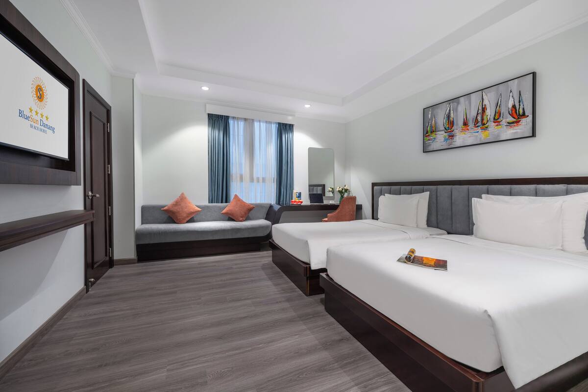A hotel room with two beds, a sofa, a desk, and a large window with curtains.