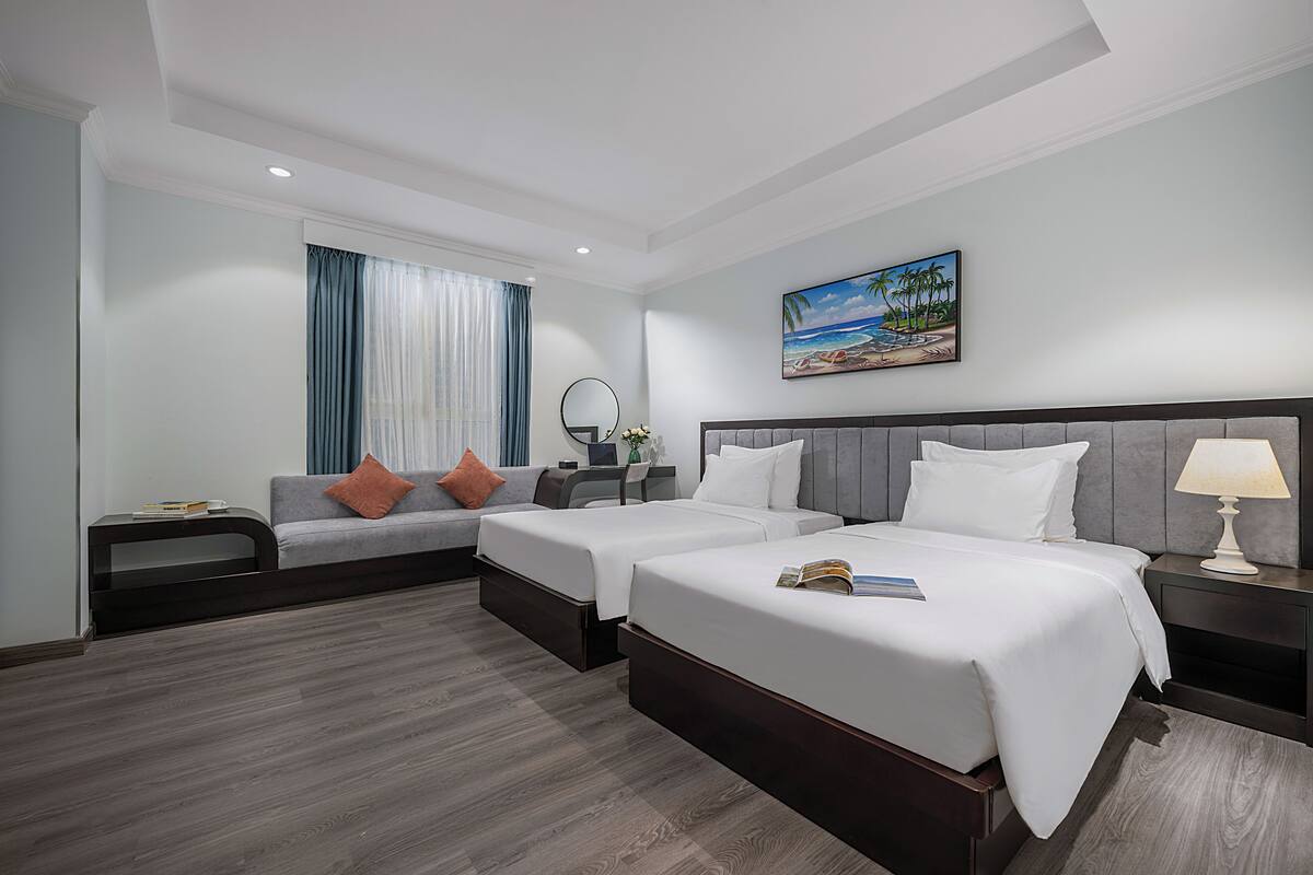 A hotel room with two beds, a sofa, a desk, and a painting on the wall.
