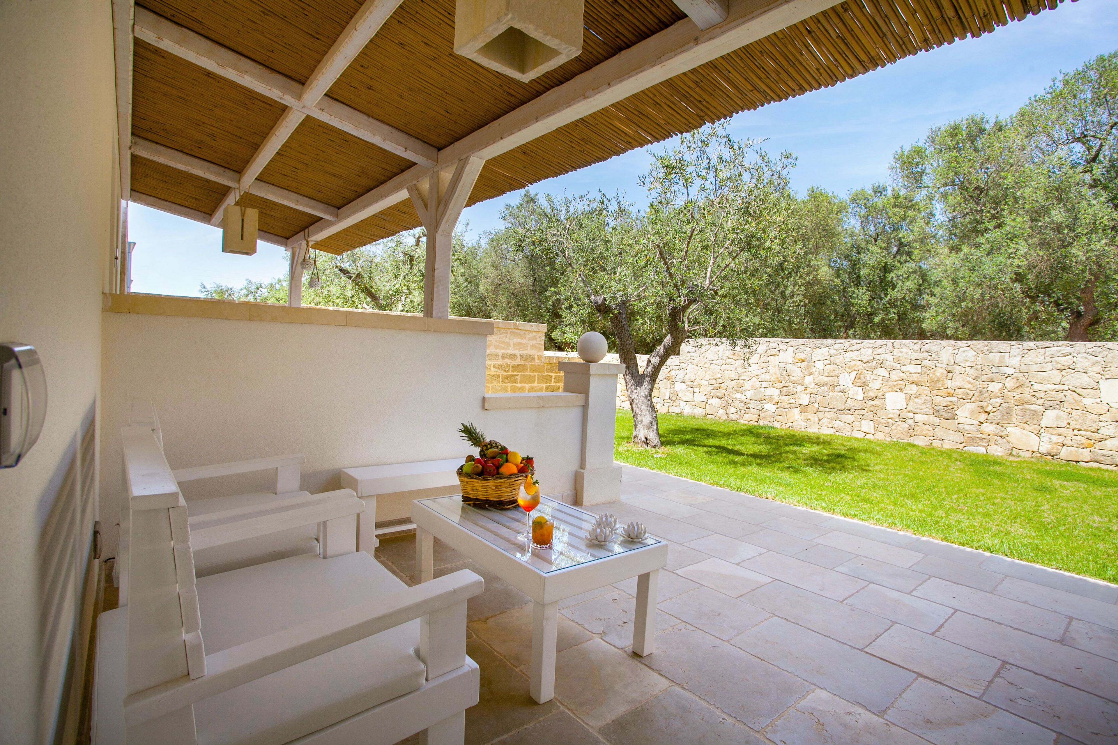 Un patio al aire libre con una mesa blanca, bancos y un muro de piedra.