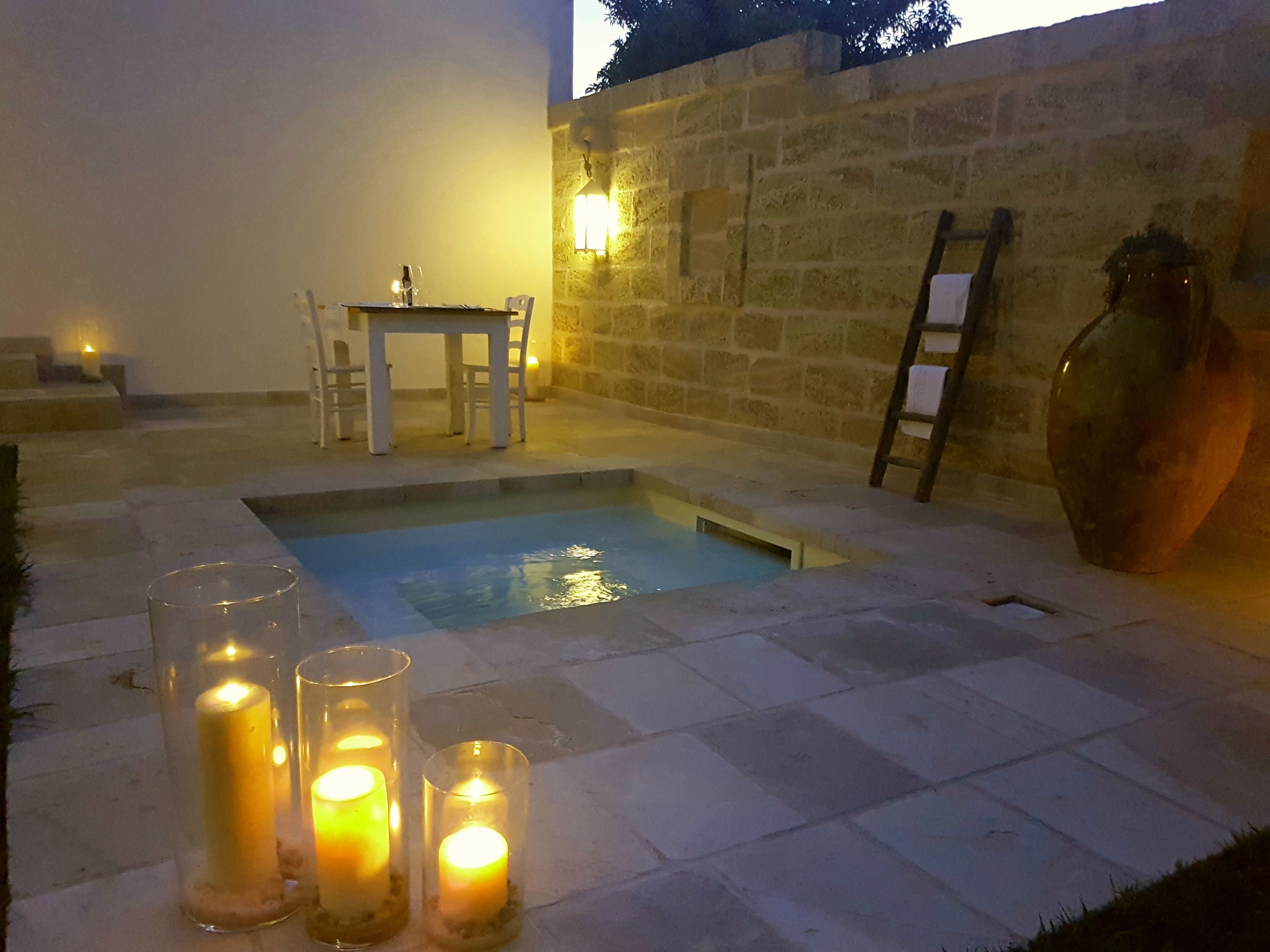A swimming pool with candles, a table, and chairs in a stone-walled area.