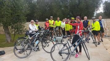 Un grupo de ciclistas reunidos alrededor de bicicletas en un entorno al aire libre, con muros de piedra y árboles al fondo.