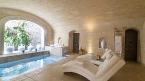 Un espacio de spa con pared de piedra, piscina, sofá de cuero blanco y ventana con plantas.