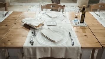 Mesa de comedor dispuesta con mantel blanco, platos, cubiertos y copas de vino, lo que sugiere un ambiente de cena formal.