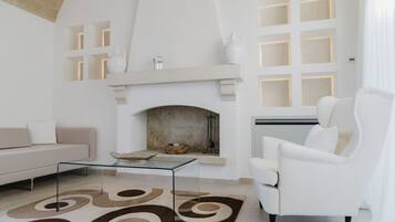 Un moderno salón con chimenea, muebles blancos y una mesa de centro de vidrio.