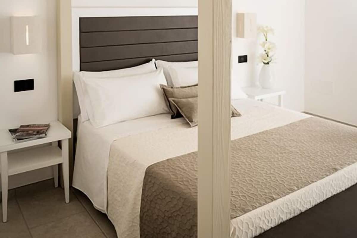 A four-poster canopy bed with a dark headboard, white bedding, and a bedside table with a lamp.