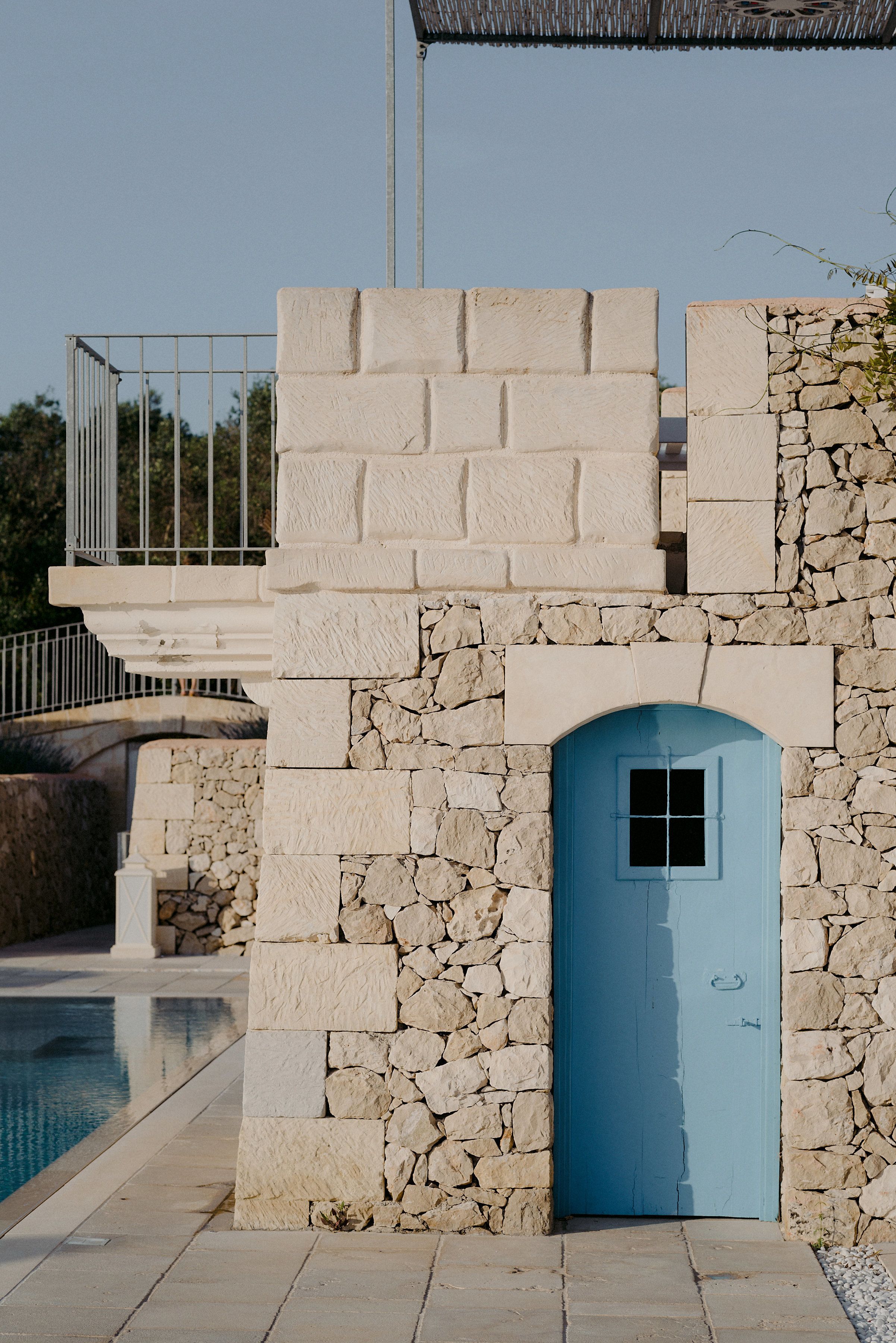 Ein Steinhaus mit einer blauen Tür, einem Pool und einer Brücke im Hintergrund.