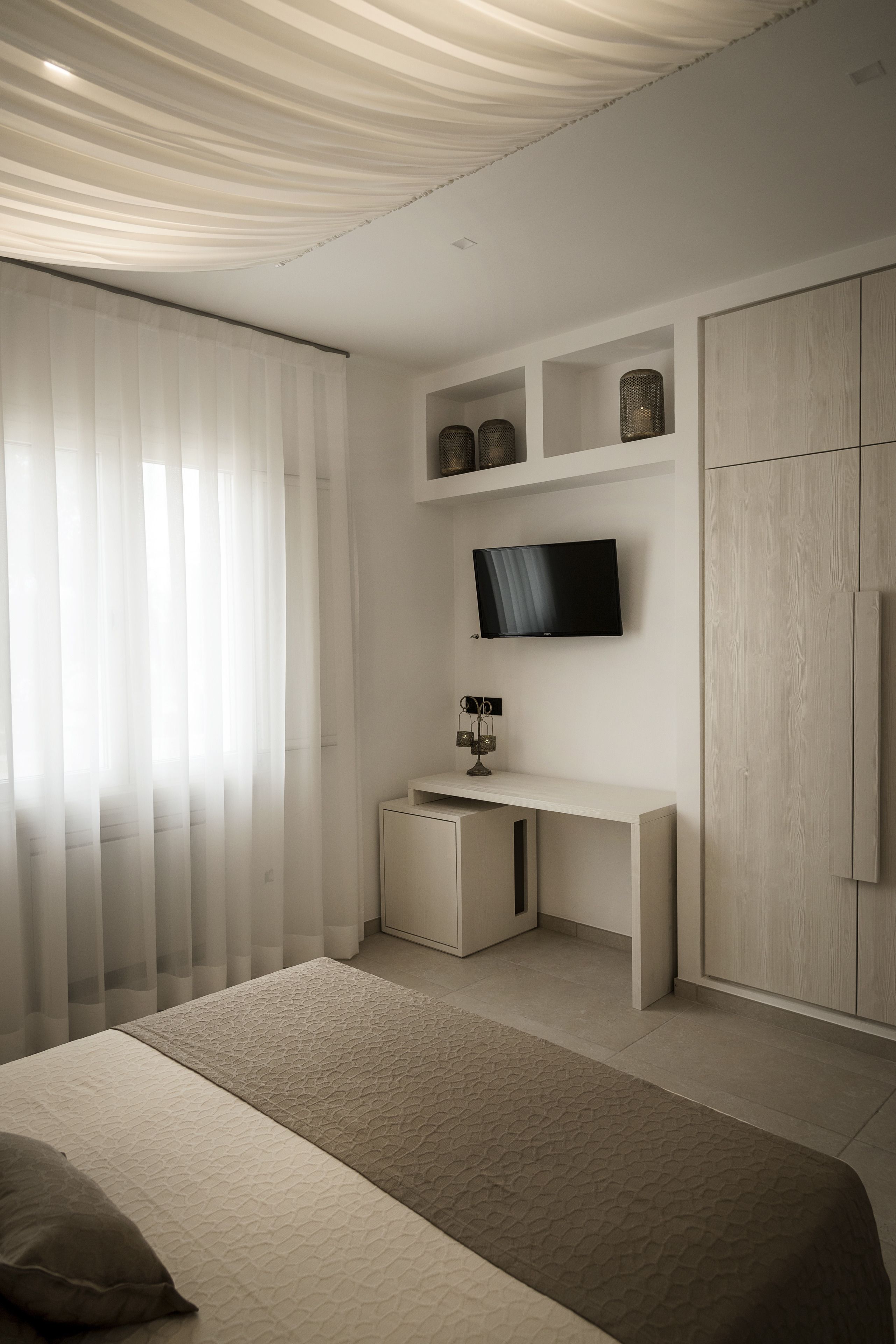 A modern bedroom with a bed, a TV mounted on the wall, a desk, and a wardrobe.