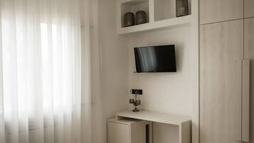 A modern bedroom with a bed, a TV mounted on the wall, a desk, and a wardrobe.