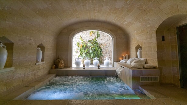 Un área de spa con un arco de piedra, un jacuzzi y jarrones decorativos.