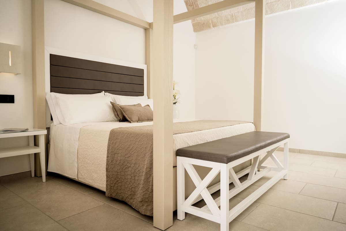 A bedroom with a bed, a bench, a nightstand, and a wall-mounted lamp.