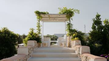 Una scala in pietra conduce a un arco in legno bianco, adornato da vegetazione.