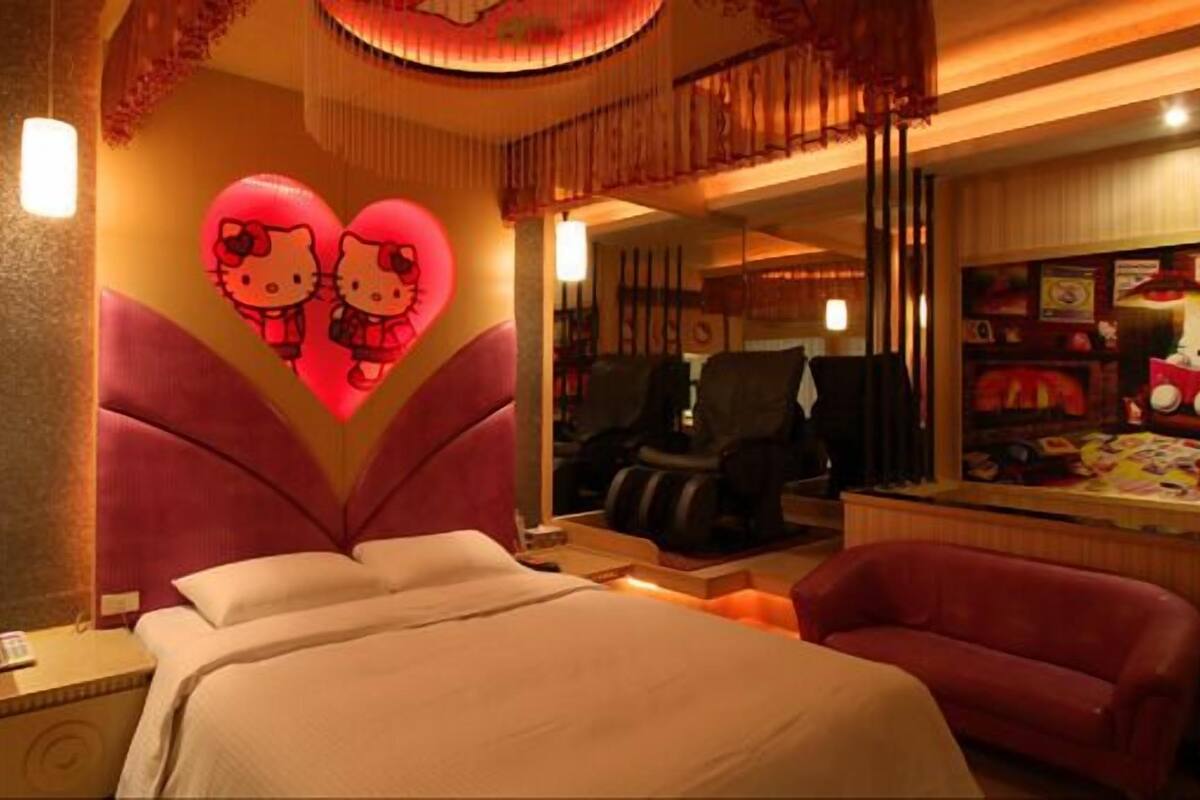 A hotel room with a large bed, a red sofa, and a wall decorated with Hello Kitty-themed items.