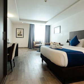 Une chambre d’hôtel avec un lit, un bureau, une chaise, une petite table et une fenêtre avec des rideaux.