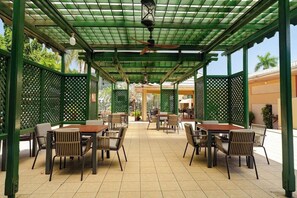 Un espace extérieur aménagé en terrasse, avec des tables et des chaises, un ventilateur de plafond et une structure en treillis végétal.