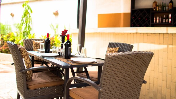 An outdoor dining area with wicker chairs and a table set for two, featuring wine bottles and glasses. - Jam Lodge (Freetown)