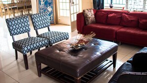 A living room with a red sofa, patterned chairs, a brown ottoman, and a decorative bowl on the ottoman. - Jam Lodge (Freetown)