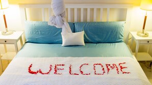 A bed with a white headboard, blue pillows, and a white bedspread with red text spelling "WELCOME". - Jam Lodge (Freetown)