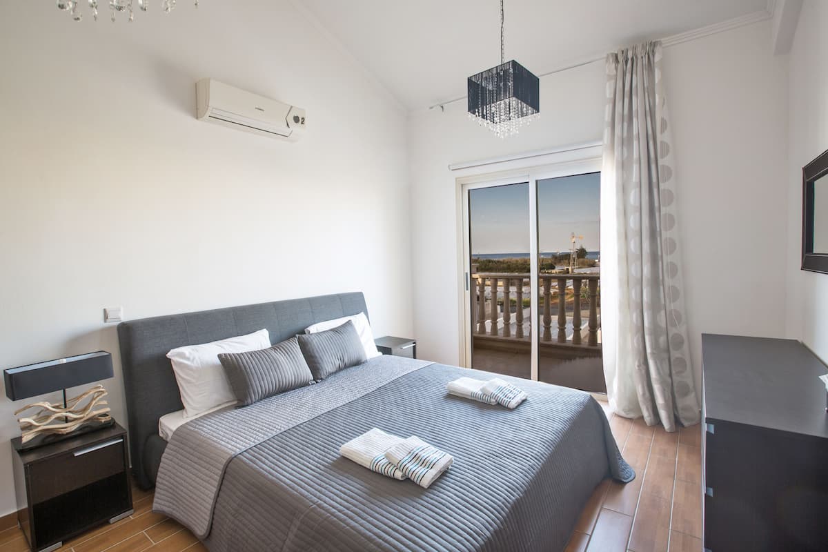 Un dormitorio moderno con una cama grande, una mesita de noche, un aparador y un balcón con vistas.