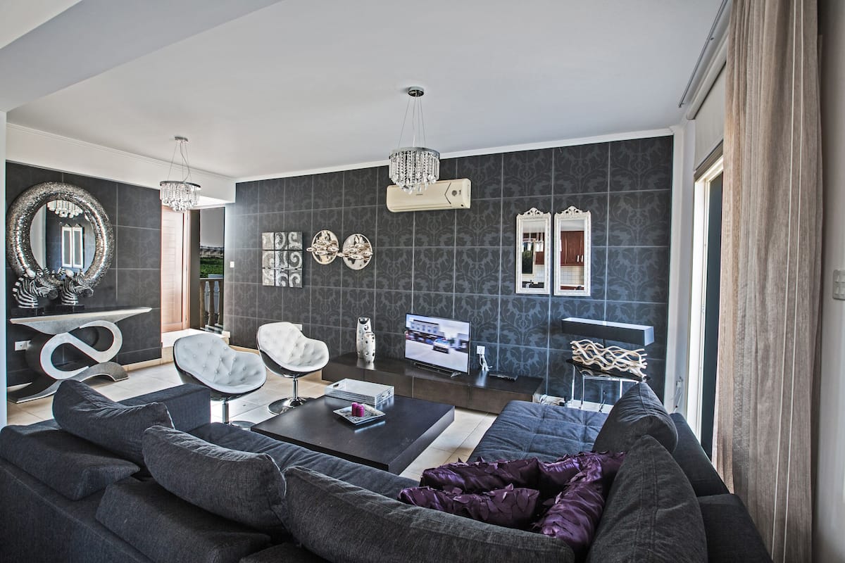 Una sala de estar moderna con un sofá gris oscuro, una silla blanca, una mesa de centro y una televisión.