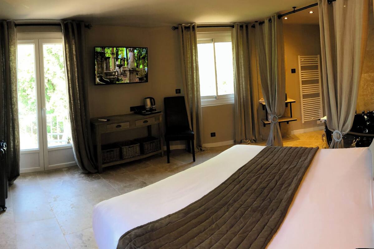 Habitación de hotel con una cama grande, un escritorio con silla, televisor y ventana con cortinas.