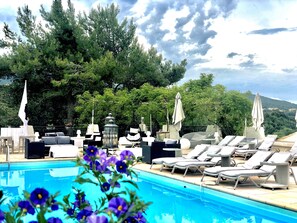 Zona de piscina con sillones de descanso y sombrillas, rodeada de árboles y vista a un paisaje montañoso.